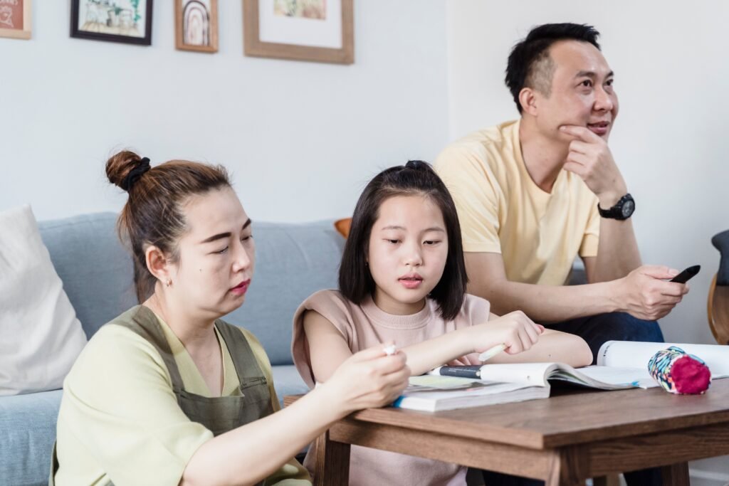 Vai trò của phụ huynh trong quá trình học trực tuyến của trẻ A family helping their daughter with homework in the living room, promoting togetherness.